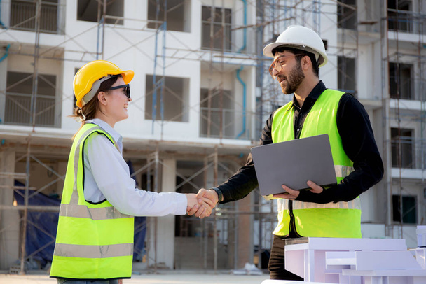 Csapatépítész vagy mérnök tartja laptop keres modell ház és ezzel megállapodást, miközben kézfogás együtt építési területen, vállalkozó és partner megbeszélés és tervezés az ingatlan. - Fotó, kép