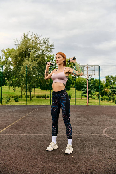 Una mujer decidida en ropa deportiva sosteniendo dos pesas en un tribunal vibrante - Foto, Imagen