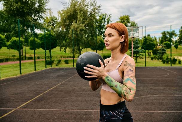 Una mujer en ropa deportiva, sosteniendo la pelota de la medicina, entrena al aire libre con determinación y motivación - Foto, Imagen