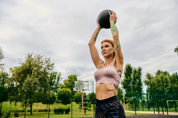 Женщина в спортивной одежде, держит в руках медицинский мяч, тренируется на открытом воздухе с мотивацией - Фото, изображение