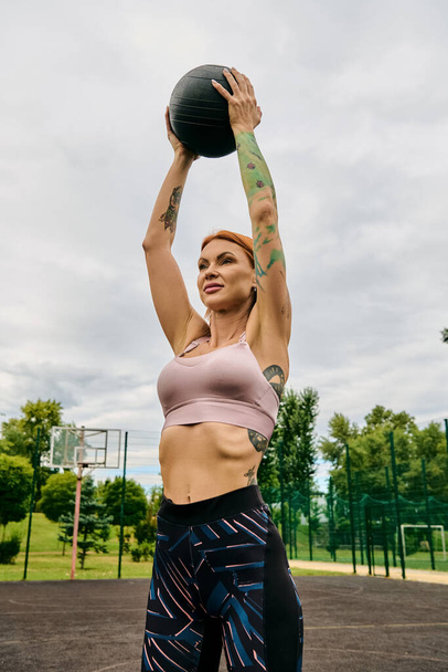Spor kıyafetli bir kadın, elinde sağlık topu, dışarıda antrenman yapıyor. - Fotoğraf, Görsel