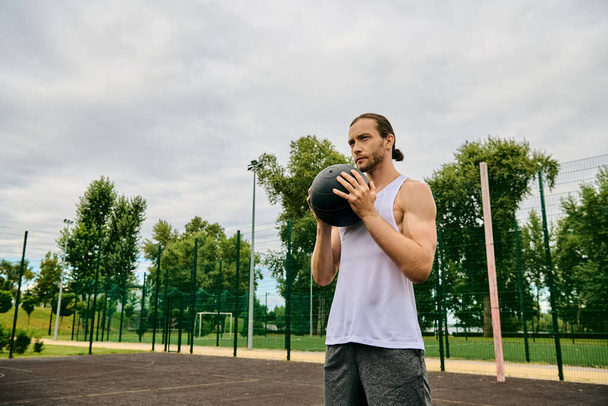 Un hombre en ropa deportiva sostiene una pelota en la cancha, mostrando determinación y motivación para el juego por delante. - Foto, Imagen