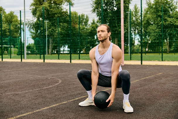 Un homme en tenue de sport est assis sur un court, tenant une balle, réfléchissant à son prochain mouvement dans le jeu. - Photo, image