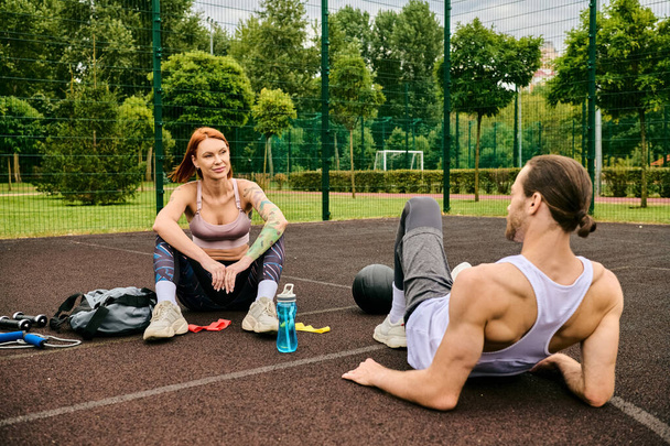 A man and a woman in sportswear sit on a basketball court, sharing determination and motivation as they exercise together. - Photo, Image