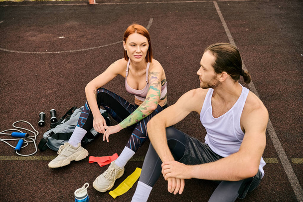 Ένας άνδρας και μια γυναίκα στα αθλητικά, ξεκουράζονται σε ένα γήπεδο μπάσκετ, αποπνέοντας αποφασιστικότητα και κίνητρο.. - Φωτογραφία, εικόνα