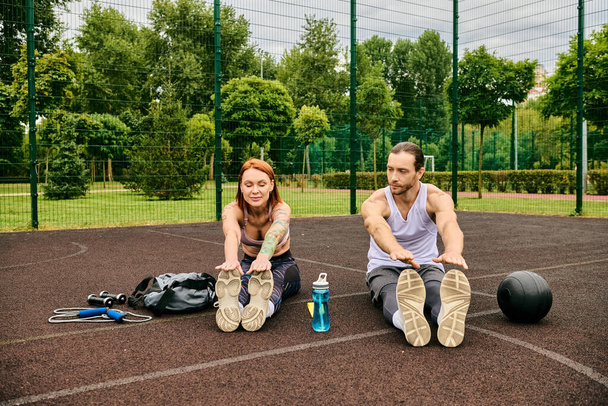 Um homem e uma mulher determinados, ambos em sportswear, sentam-se juntos em uma quadra de basquete, alcançam seus objetivos de fitness. - Foto, Imagem