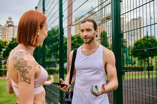 Spor giyim sektöründe bir erkek ve bir kadın çitin yanında durur. Açık hava antrenmanında kişisel eğitimle motive olurlar.. - Fotoğraf, Görsel