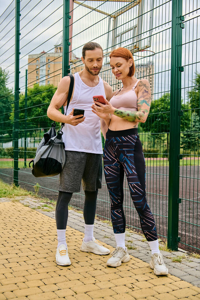 Mężczyzna i kobieta w odzieży sportowej stoją obok siebie na zewnątrz, trzymając smartfony - Zdjęcie, obraz