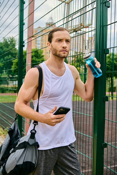 Un homme se tient à côté d'une clôture, tenant un téléphone portable, absorbé dans son contenu. - Photo, image