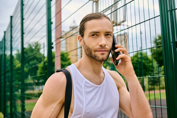 Een vastberaden man in sportkleding praat op zijn mobiele telefoon in een buitenomgeving terwijl hij zijn kracht en focus toont. - Foto, afbeelding