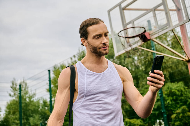 Un hombre sostiene un teléfono celular frente a un aro de baloncesto. - Foto, imagen