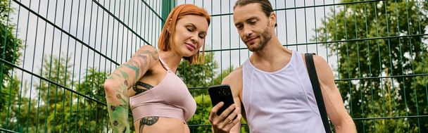 Un uomo e una donna in abbigliamento sportivo stanno insieme all'aperto, utilizzando lo smartphone - Foto, immagini
