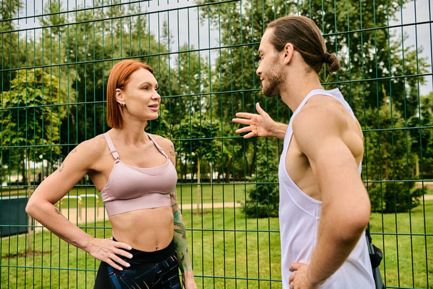 Μια αποφασισμένη γυναίκα μιλάει με έναν προσωπικό γυμναστή ενώ γυμνάζεται μπροστά από ένα φράχτη στην ύπαιθρο. - Φωτογραφία, εικόνα
