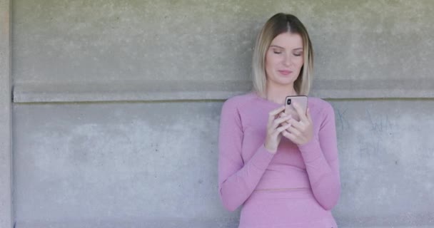 Dieses Archivmaterial zeigt eine junge Frau in einem stylischen rosafarbenen Kleid, die ihr Smartphone gegen eine minimalistische Betonwand hält. Die Einfachheit des Hintergrunds steht im Kontrast zur Modernität der mobilen - Filmmaterial, Video