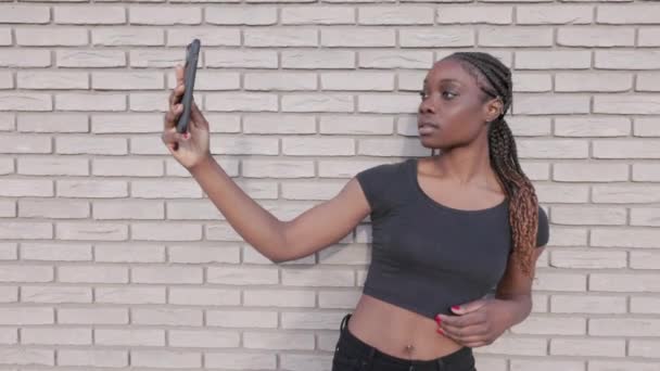 Cette séquence montre une jeune femme soucieuse de sa santé en tenue de sport, vérifiant son application de fitness sur un smartphone contre un mur de briques blanches. La vidéo capture un moment de préparation ou de révision - Séquence, vidéo