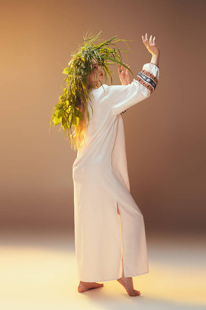 Eine junge Frau im weißen Kleid schmückt ihren Kopf mit einer Pflanzenkrone und verkörpert eine skurrile, märchenhafte Ästhetik in einem Atelier-Setting. - Foto, Bild