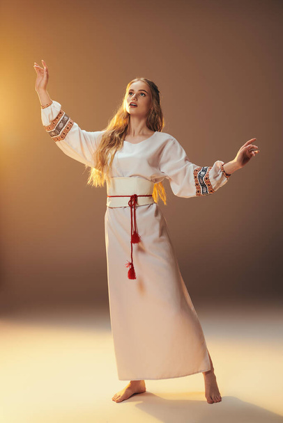 Молодая женщина в традиционном белом платье обнимает мир протянутыми руками в обстановке сказочно-фантастической студии. - Фото, изображение