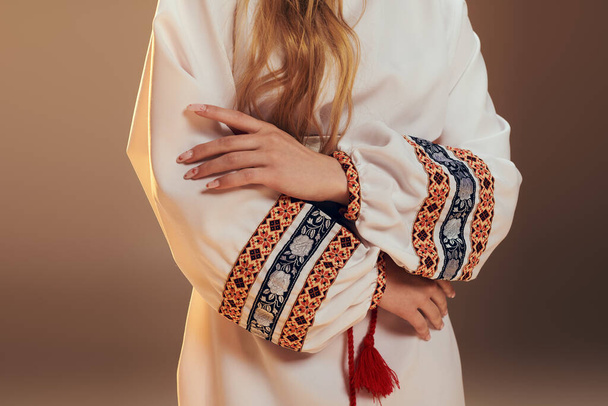 Um jovem mavka adornado em um vestido branco com uma impressionante borla vermelha, exalando um ar de mística em um estúdio. - Foto, Imagem