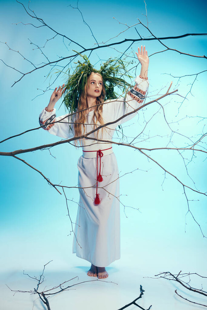 Een jonge vrouw in een traditionele outfit, versierd met een sprookjeskrans, staat gracieus voor takken. - Foto, afbeelding
