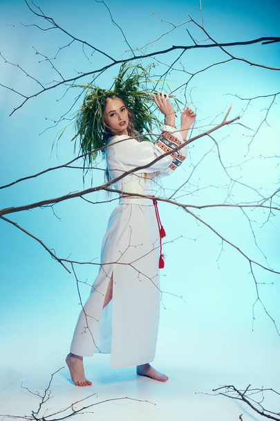 Μια νεαρή γυναίκα με λευκό φόρεμα κρατά με χάρη ένα ευαίσθητο κλαδί, που ενσωματώνει την ηρεμία και τη σύνδεση με το φυσικό κόσμο. - Φωτογραφία, εικόνα