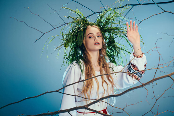 Una giovane donna vestita da mavka, che indossa una corona, in piedi davanti a un albero in uno studio a tema fata e fantasia. - Foto, immagini