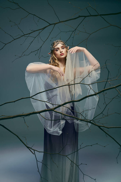 Eine junge Frau in einem weißen Kleid, die eine Fee oder Elfe verkörpert, steht königlich neben einem majestätischen Baum in einem Atelier-Ambiente. - Foto, Bild