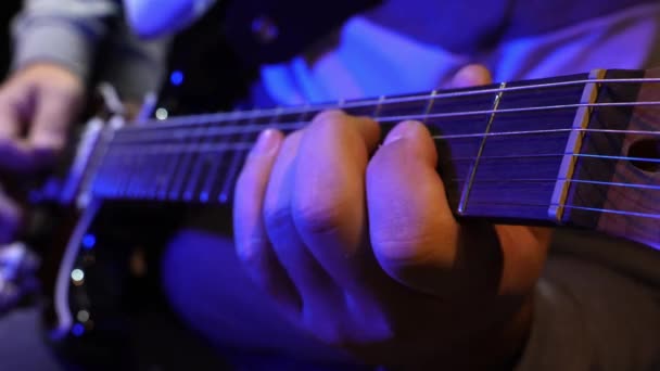 Incantevole primo piano del musicista che suona la chitarra elettrica sotto l'illuminazione blu, strumentando abilmente corde e suonando accordi su tasti su tastiera. - Filmati, video