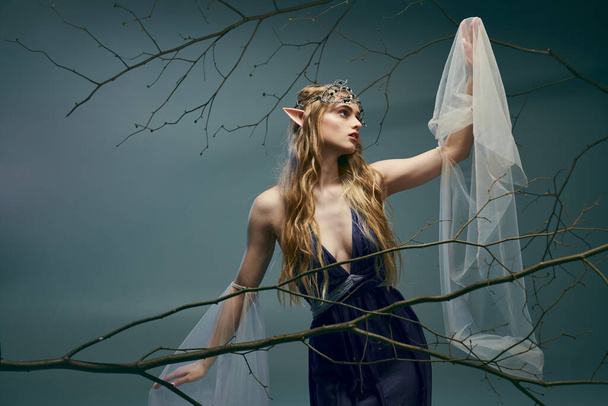 Een jonge vrouw met een sluier op haar hoofd staat gracieus voor een weelderige boom, belichaamt de essentie van een sprookjesprinses. - Foto, afbeelding