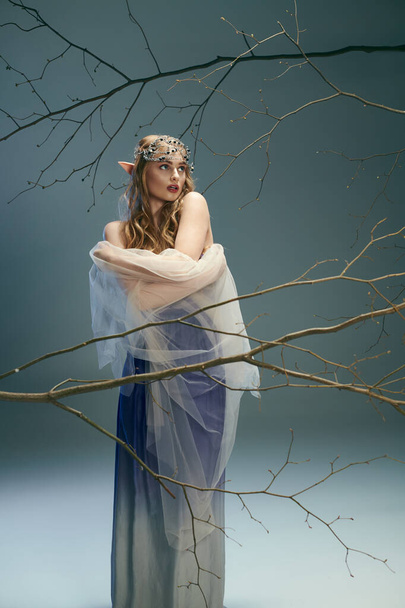 Una giovane donna in abito blu in piedi con grazia di fronte a un albero maestoso, che incarna l'essenza di una principessa fata. - Foto, immagini
