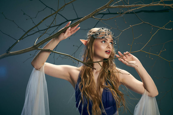 Una joven vestida con un vestido azul fluido se levanta con gracia junto a un majestuoso árbol en un entorno de fantasía. - Foto, imagen
