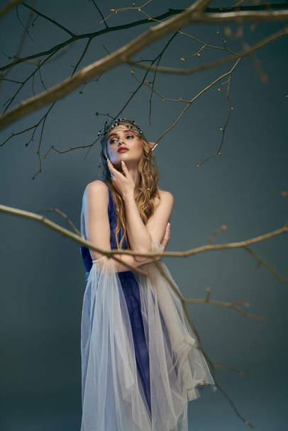 Молодая женщина в сине-белом платье изящно стоит рядом с деревом в сказочной обстановке. - Фото, изображение