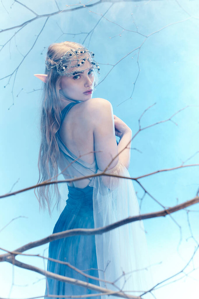 Młoda kobieta w płynącej niebieskiej sukience stoi z wdziękiem na drzewie, ucieleśniając księżniczkę w świecie fantazji. - Zdjęcie, obraz