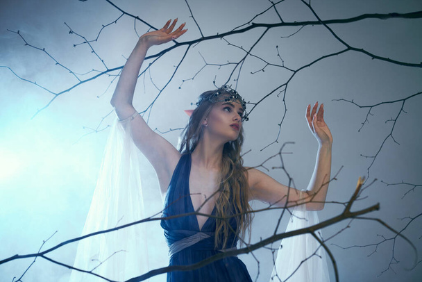 Молодая женщина в синем платье, грациозно стоящая перед величественным деревом, источая воздух фантазии и магии. - Фото, изображение
