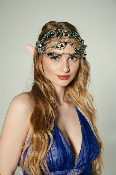 Młoda kobieta w niebieskiej sukience z koroną na głowie, ucieleśniająca esencję księżniczki w mistycznym, studyjnym otoczeniu. - Zdjęcie, obraz