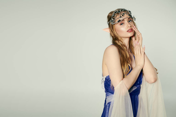 A young woman embodies an elf princess in a blue dress with a delicate veil in a whimsical studio setting. - Photo, Image