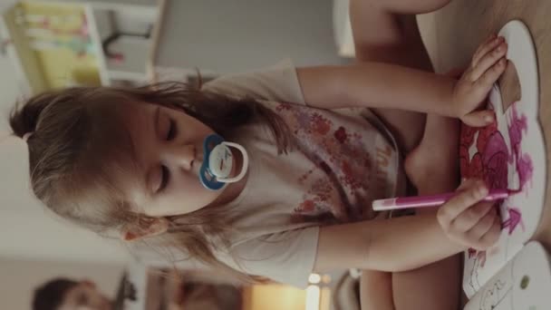 Симпатична маленька дівчинка з двох років смокче соску, малюючи з рожевим маркером в альбомі в дитячій кімнаті вдома. Освітня діяльність для - Кадри, відео