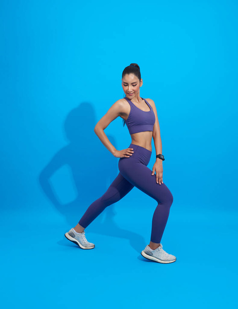 Азиатская фитнесс-спортсменка занимается растяжкой. Полный снимок молодой женщины разогрева упражнения изолированы на синем фоне. Растяжка и мотивация - Фото, изображение