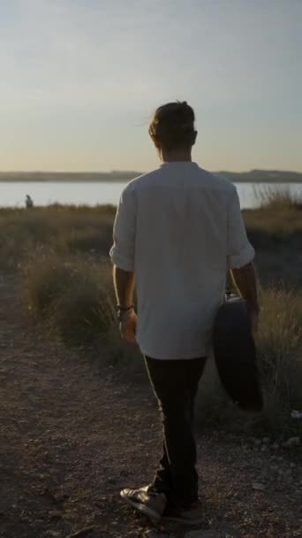 De man met gitaar draaiend in een cirkel tegen de prachtige zonsondergang - Verticale FullHD video - Video