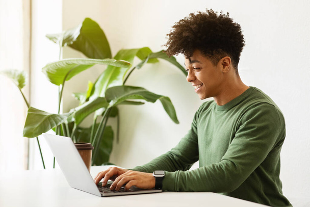 現代のライフスタイル。 フリーランス 遠隔勤務。 若いアフリカ系アメリカ人カーリーマンは,カフェでラップトップで作業し,コンピュータのキーボードを入力し,コーヒーを飲んで,スペースをコピーします. - 写真・画像