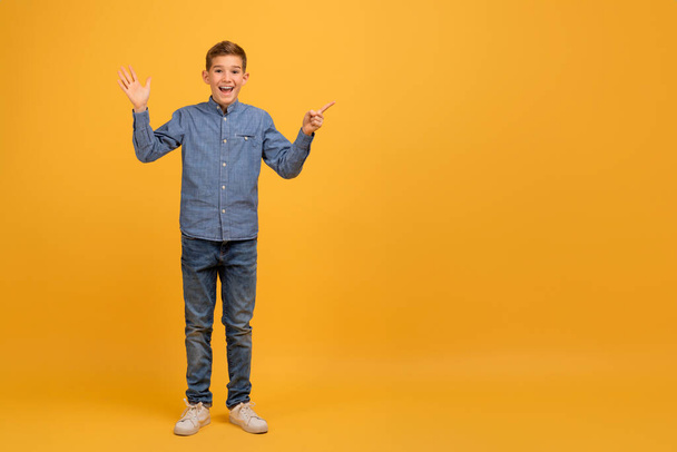 ハッピーエキサイティングなティーンボーイは指でコピースペースを指さして,あなたの広告デザインのための無料の場所を示す大喜びの十代の男性の子供,黄色の背景に立って,完全な長さ - 写真・画像