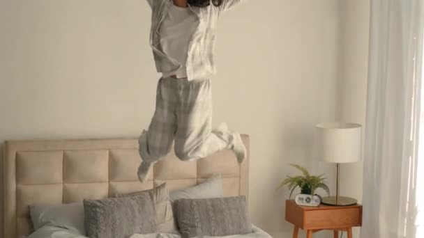 Glücklich junge kaukasische Frau springen Bett hält Smartphone Handy freudig unbeschwert fröhlich Mädchen Wochenende Freizeit zu Hause morgens Musik Schlafzimmer aufgeregt Matratze genießen Urlaub energetischen Spaß häuslichen - Filmmaterial, Video