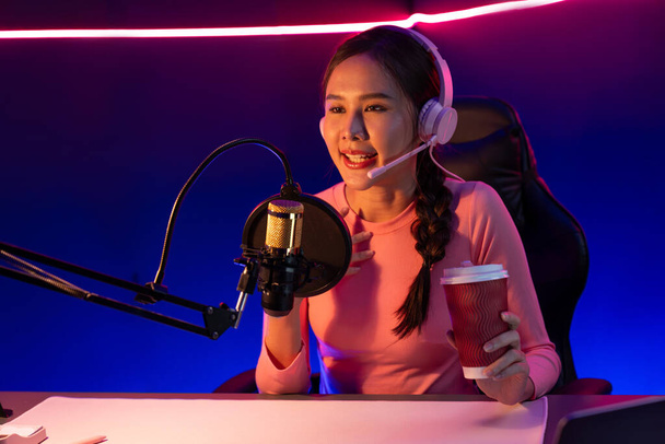 Host channel of creative broadcast listening the music on social media with listeners holding coffee up, wearing pastel color headphones, using mic radio record by camera at neon studio. Stratagem. - Photo, Image