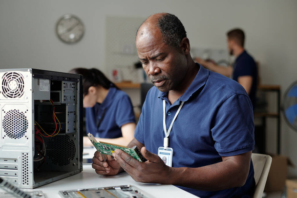 Erfahrener Techniker oder Mitarbeiter des Reparatur-Service-Büros schaut sich Computermotherboard an, während er Teile des Prozessors überprüft - Foto, Bild