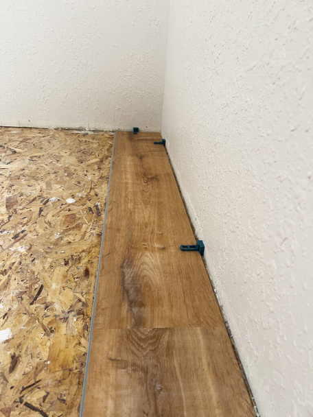 Medido cuidadosamente y espaciado uniformemente, el primer tablón de vinilo se instala expertamente contra la pared, marcando el comienzo de una renovación transformadora del piso.. - Foto, imagen