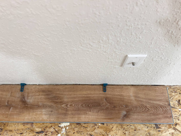 Huolellisesti mitattu ja tasaisin välein, ensimmäinen vinyyli lankku on asiantuntevasti asennettu seinää vasten, mikä merkitsee alkua muuntava lattia remontin. - Valokuva, kuva