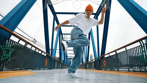 Un danseur de pause professionnel exécute des pas de danse de rue au pont. Asiatique hipster porter casque lors de la pose de gel. Break dancer, street dancer freestyle concept. Sport de plein air 2024. Brillamment. - Photo, image