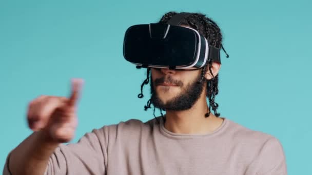 een man uit het Midden-Oosten met een virtual reality-headset, die gebaren maakt. BIPOC persoon met behulp van high tech futuristische moderne VR gadget, geïsoleerd over blauwe studio achtergrond, camera B - Video
