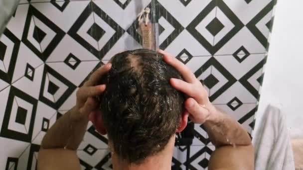 Mężczyzna pod prysznicem myjący włosy w łazience w domu. Nierozpoznawalna osoba zza płukania szamponu i odżywki z włosów w ciepłej kąpieli z nowoczesną łazienką. - Materiał filmowy, wideo