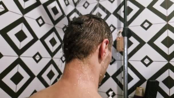 Muž ve sprše myje vlasy sprchující se doma v koupelně. Nerozpoznatelná osoba zezadu oplachování šampon a kondicionér z vlasů v teplé koupeli s moderní koupelnou. - Záběry, video