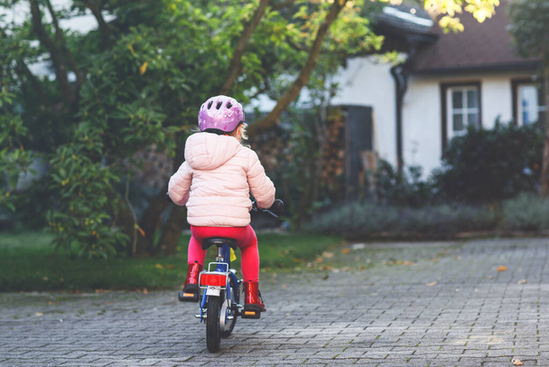 Pequeña niña preescolar montar en bicicleta. Un chico en bicicleta al aire libre. Feliz niña disfrutando de paseo en bicicleta en su camino a la escuela en el cálido día de verano. Aprendizaje preescolar para equilibrarse en bicicleta en casco seguro - Foto, imagen